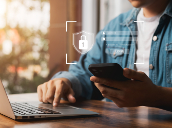 Mensch arbeitet an Endgeräten und Login-Fenster ist halbtransparent über Smartphone platziert.