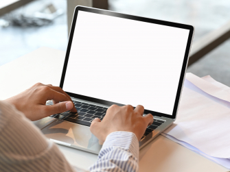 Laptop auf Schreibtisch mit weißem Bildschirm, davor sitzt eine Person